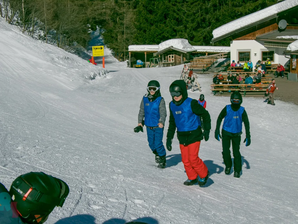 Drei Jugendliche gehen mit Snowboards über die Piste.